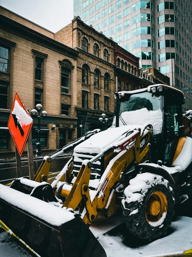 A snow-covered tractor excavator on a Toronto city street during winter roadworks.